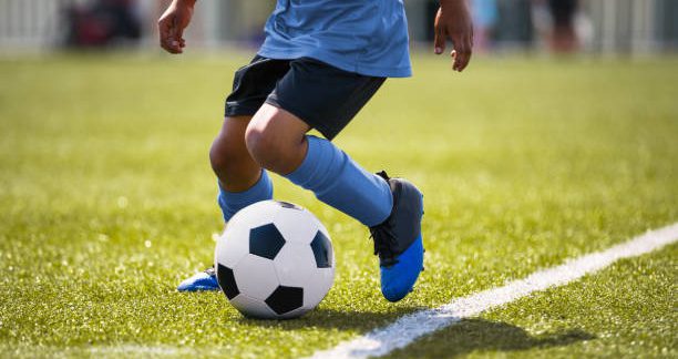 African American young boy playing soccer in a stadium pitch. Child running with soccer ball along the field white sideline. Junior soccer background
